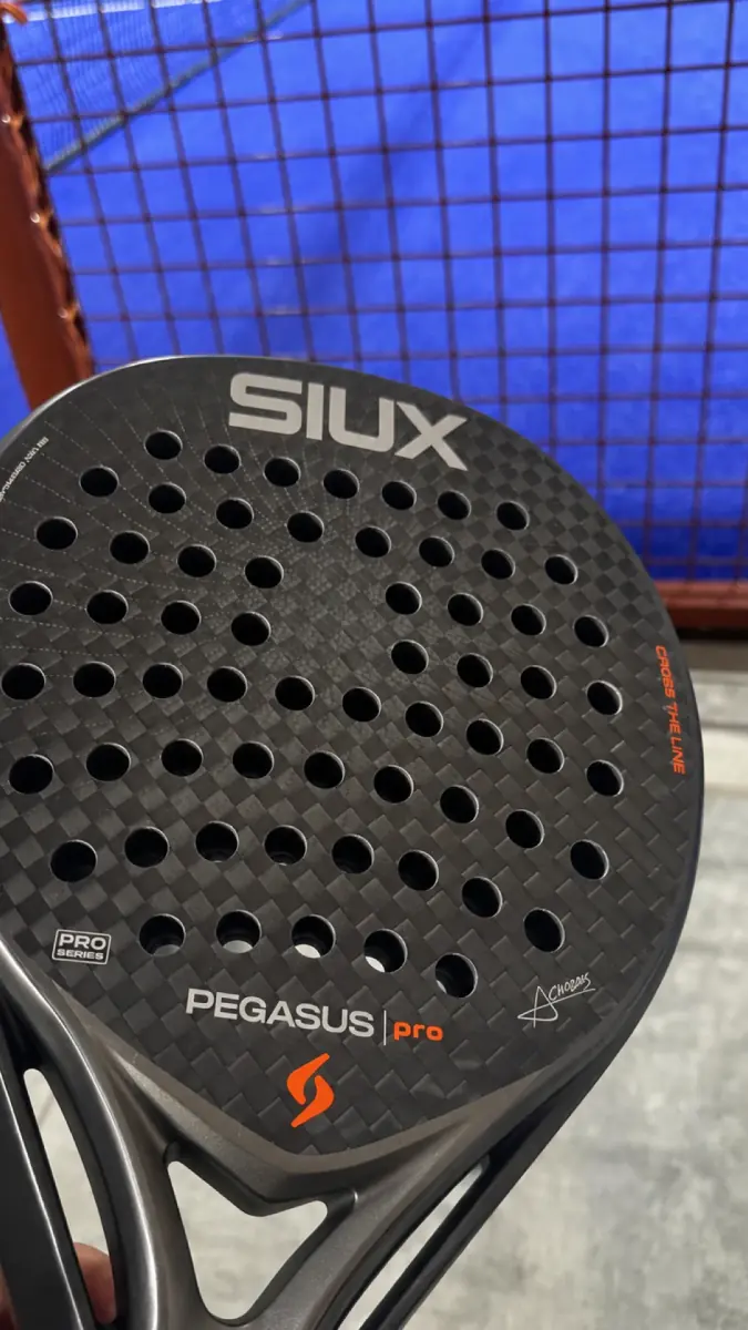 A black carbon padel racket held up against the court net